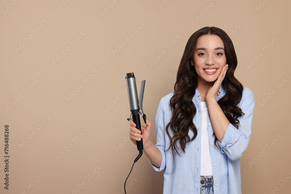 Happy woman with curling hair iron on beige background. Space for text Happy woman with curling hair iron on beige background. Space for text