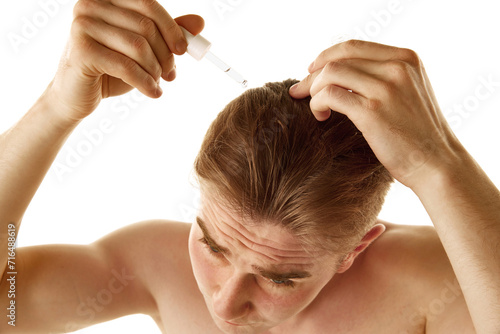Young shirtless man taking care after health, applying head oil, serum isolated over white background. Concept of male beauty, skin care, cosmetology and cosmetics, health