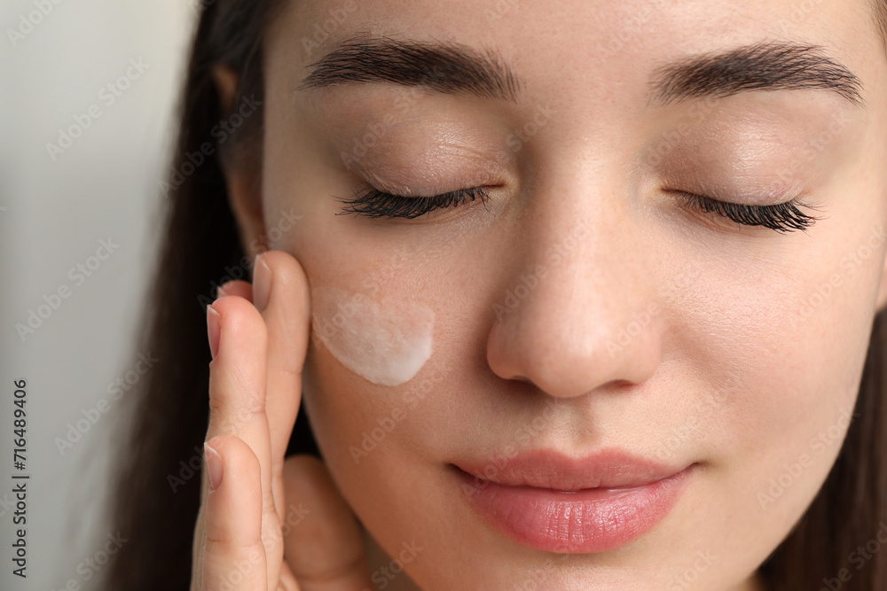 Young woman with dry skin applying cream onto her face on blurred background, closeup Young woman with dry skin applying cream onto her face on blurred background, closeup