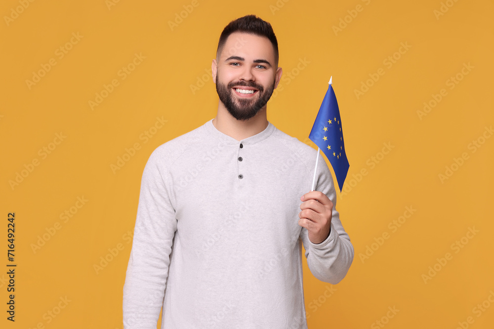 Young man holding flag of European Union on orange background Young man holding flag of European Union on orange background