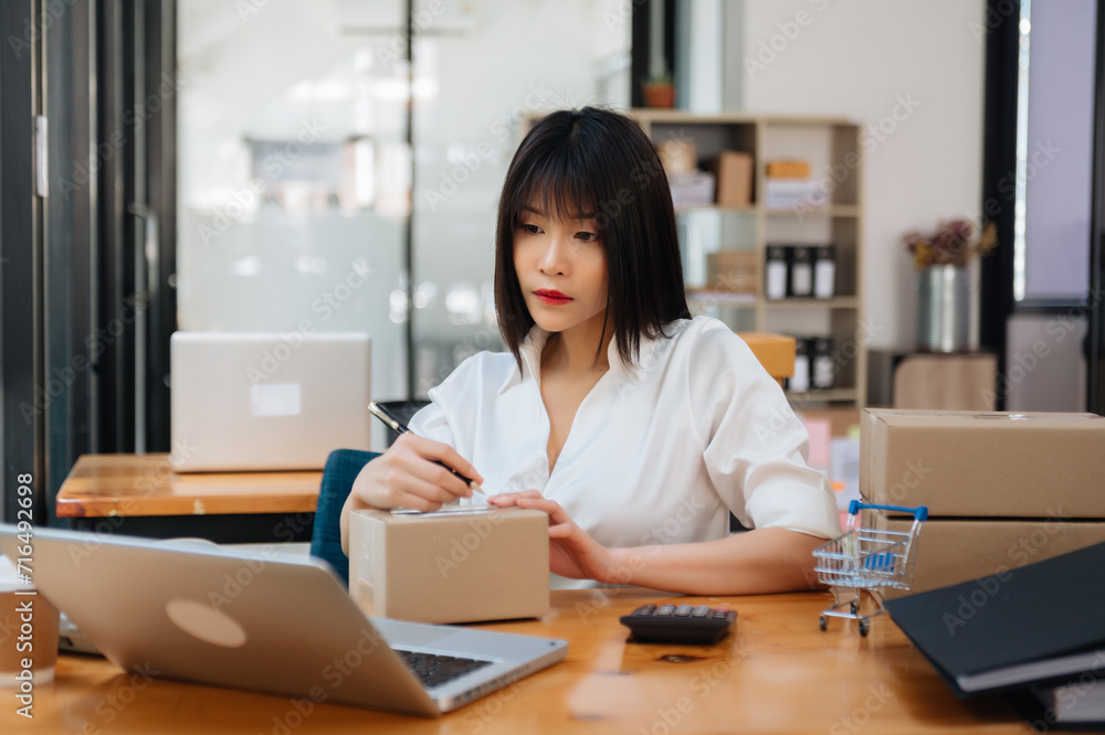 Young business owner woman prepare parcel box and standing check online orders for deliver to customer on tablet, laptop Shopping Online.. Young business owner woman prepare parcel box and standing check online orders for deliver to customer on tablet, laptop Shopping Online..