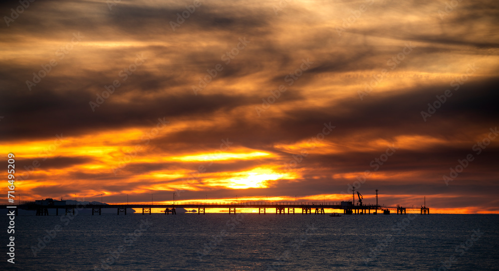 A sunset over the sea with pier in silhouette