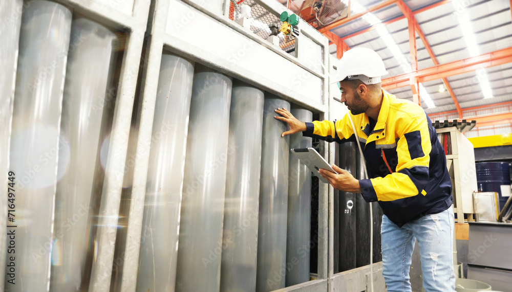 Male technician engineer wearing helmet holding tablet inspects the workplace stores oxygen tanks pressure tanks and checks safety working pressure safe storage area in sheet metal industry factory. Male technician engineer wearing helmet holding tablet inspects the workplace stores oxygen tanks pressure tanks and checks safety working pressure safe storage area in sheet metal industry factory.