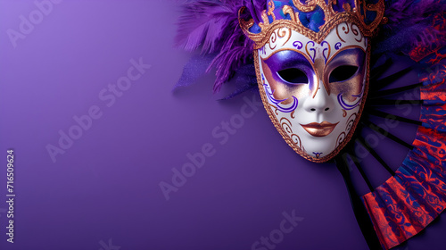 purple and yellow venetian or masquerade mask, feather, confetti and hand fan. over on the purple background. free space for text advertising. photo