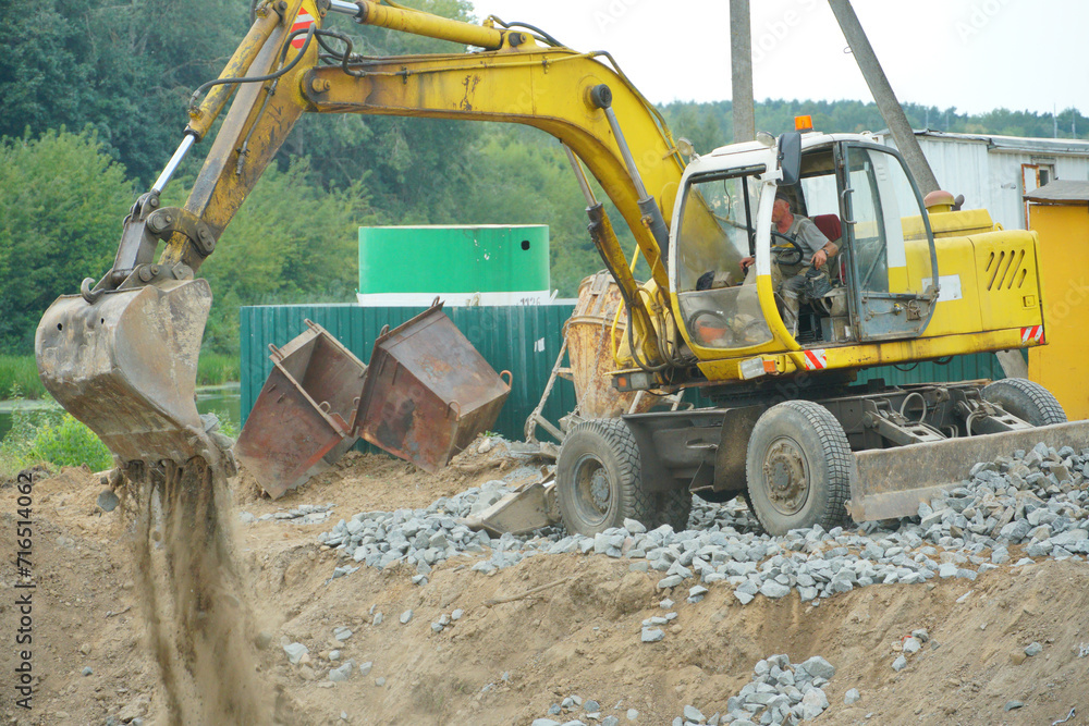 Obraz premium An excavator and other heavy construction equipment are working on the construction site. Construction of a new bridge across the river. Road works, laying of a new road.