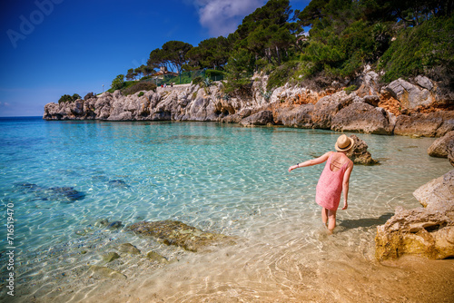 A woman in a summer dress and straw hat enjoying a stroll in the water along Cala Gat beach in Mallorca