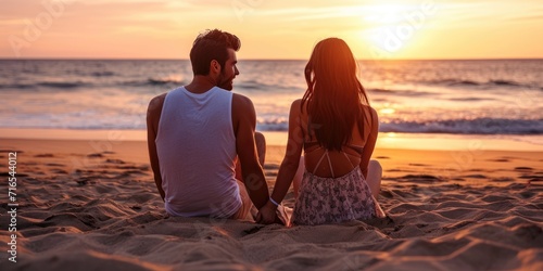 Beautiful couple sitting on the beach sand back to back and watching the sunset