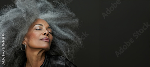 Side view at middle-aged beautiful woman with long grey hair, her eyes closed, body and face care concept. Charming mature lady stands in profile isolated on grey background