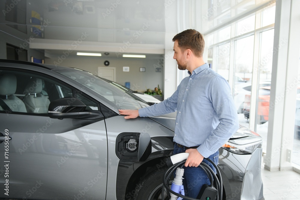 A happy man chooses a new electric car at a car dealership. The concept of buying an ecological car