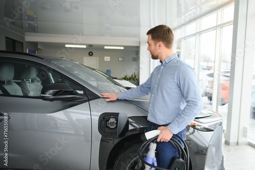 A happy man chooses a new electric car at a car dealership. The concept of buying an ecological car