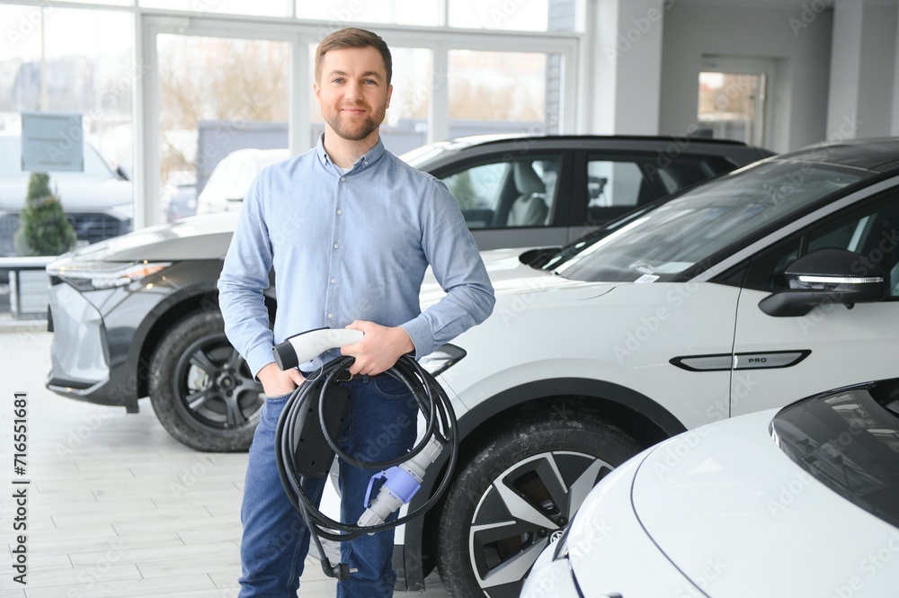 A happy man chooses a new electric car at a car dealership. The concept of buying an ecological car A happy man chooses a new electric car at a car dealership. The concept of buying an ecological car