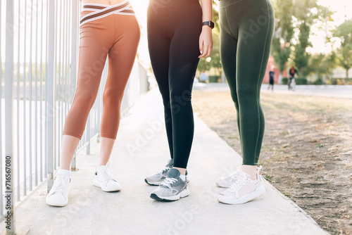 Cropped photo of three women best friends in sport leggings and sneakers standing outdoors photo