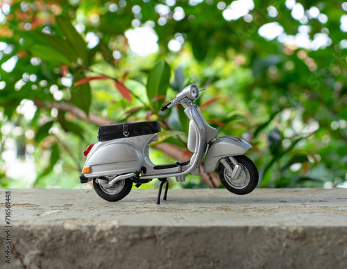 Miniature classic scooter on the cement floor with nature background. After some edits.