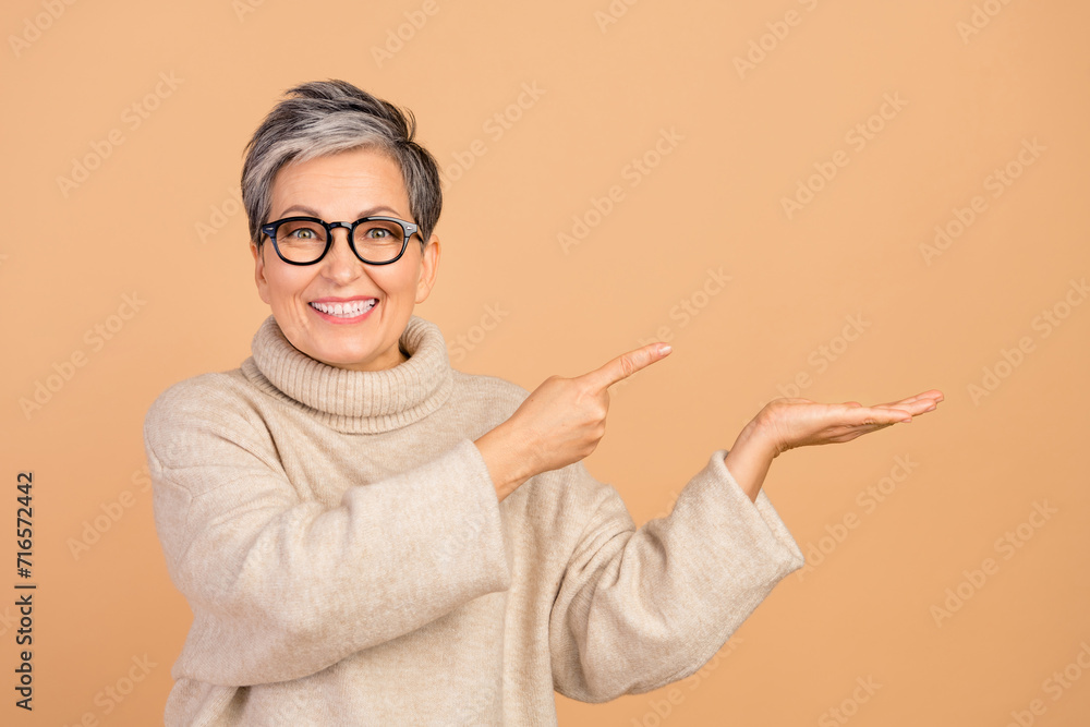 Portrait of cheerful pretty lady toothy smile direct finger arm hold empty space isolated on beige color background
