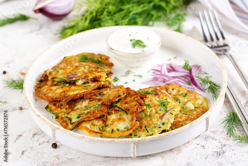 Zucchini fritters with red onions, garlic and herbs. Vegetarian zucchini pancakes and sour cream on white table.