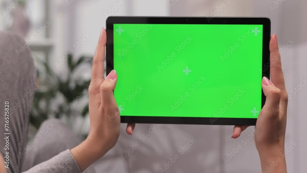 Closeup shot of girl lying on sofa using tablet in horizontal position with green screen mockup in bright room using different gestures while watching video. Closeup shot of girl lying on sofa using tablet in horizontal position with green screen mockup in bright room using different gestures while watching video.