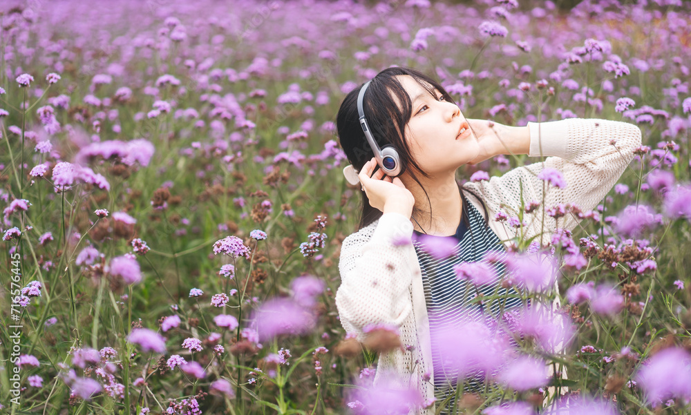 Portrait of young adult asian woman relax in wild flower listen music with headphone and dancing in self mood Portrait of young adult asian woman relax in wild flower listen music with headphone and dancing in self mood