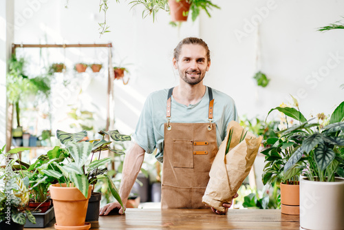 Young handsome Caucasian salesman, employee selling potted plants in a flower store.