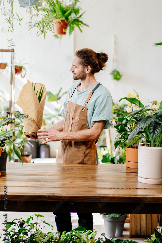 Young handsome Caucasian salesman, employee selling potted plants in a flower store.