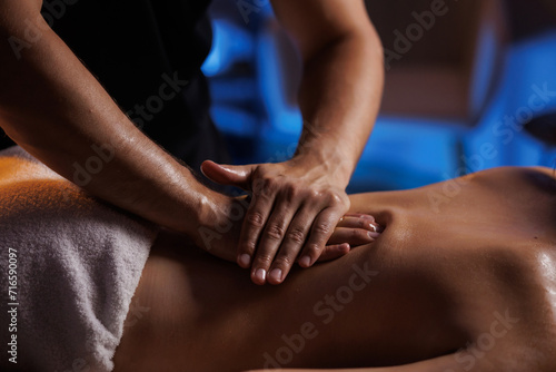 A young brunette woman receives a professional back massage in a spa salon. A beautiful naked lady in a towel with perfect skin gets a relaxing massage. The concept of luxury professional massage.