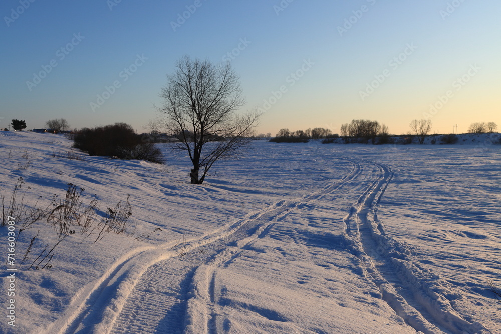 Snowmobile tracks in the snow on a frozen river at sunset on a winter evening
