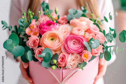 Bouquet of fresh ranunculus, roses and eucalyptus in pink  box in hands of woman florist