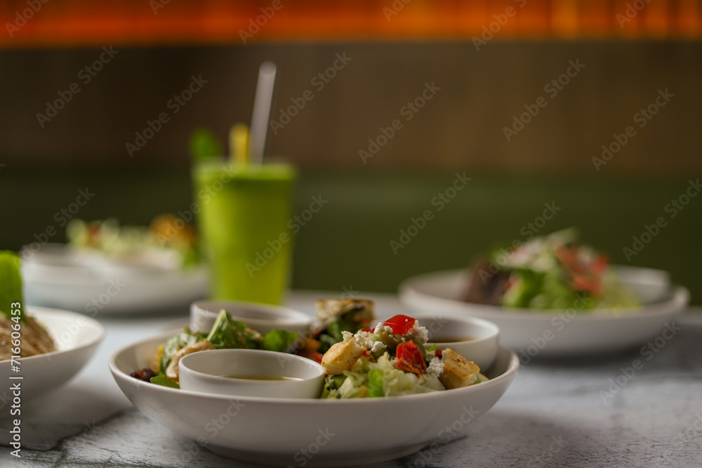 Delicious gourmet healthy chicken salad bowls and fresh mint margherita, with Spanish onion, lettuce, lemon and olive oil, served in white ceramic bowl, with seasoning and herbs on a restaurant table.