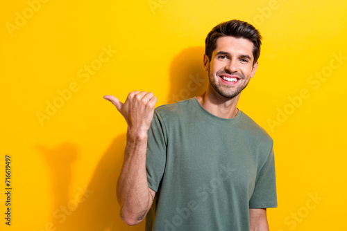 Photo of toothy beaming man with bristle dressed khaki t-shirt indicating at proposition empty space isolated on yellow color background