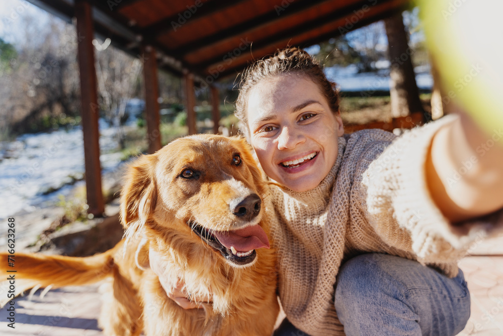 Happy young woman with her labrador retriever dog taking selfie while hugging, spending joyful time together