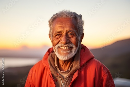 Portrait of a cheerful indian elderly man in his 90s wearing a zip-up fleece hoodie against a vibrant sunset horizon. AI Generation