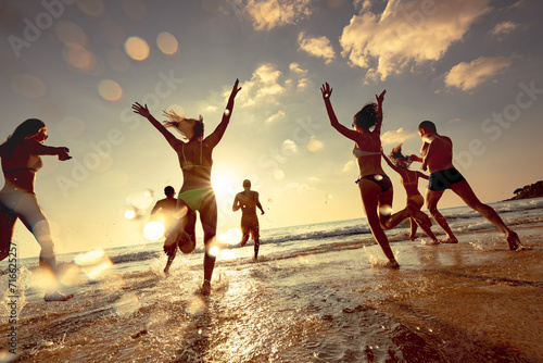 Big group of happy young friends are having fun, runs and jumps at sunset sea beach. Tropical vacations concept