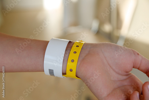 close-up of yellow plastic bracelet on the girl arm of child clinic patient, check tape with entry number on hand of teenager girl, event ticket concept photo