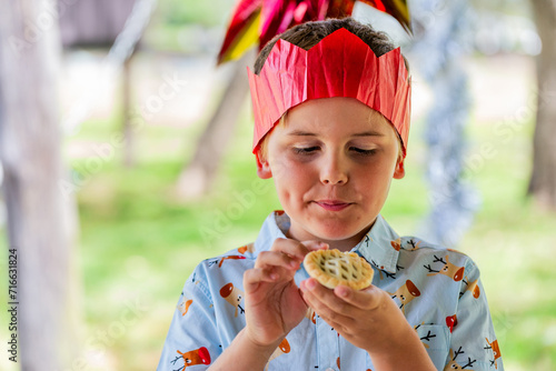Aussie child staring hungrily at fruit mince pie in hands while wearing paper crown at Christmas photo