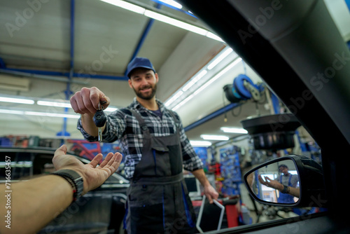 Sealing the deal with a smile: A white mechanic passes car keys to a happy customer, embodying quality service and customer satisfaction in the workshop. photo