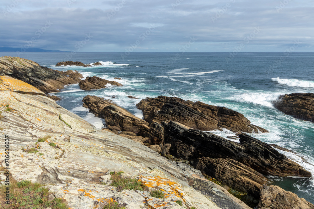 a rugged coastline with jagged rocks and turbulent ocean waves under a partly cloudy sky, exuding wild, natural beauty