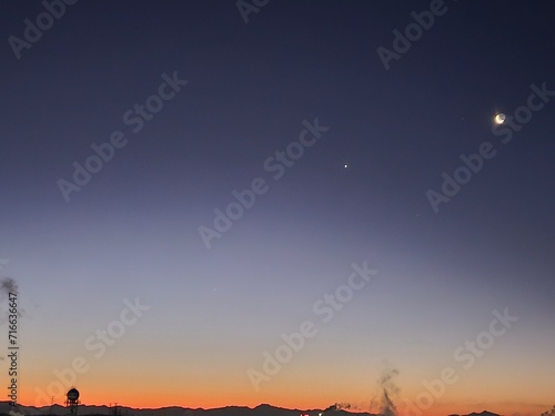 The crescent moon and Venus hover above the factories at dawn in the city.
