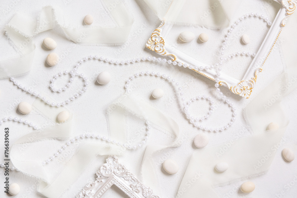 Obraz premium White frames, pearls, pebbles and silk ribbons top view on a white table