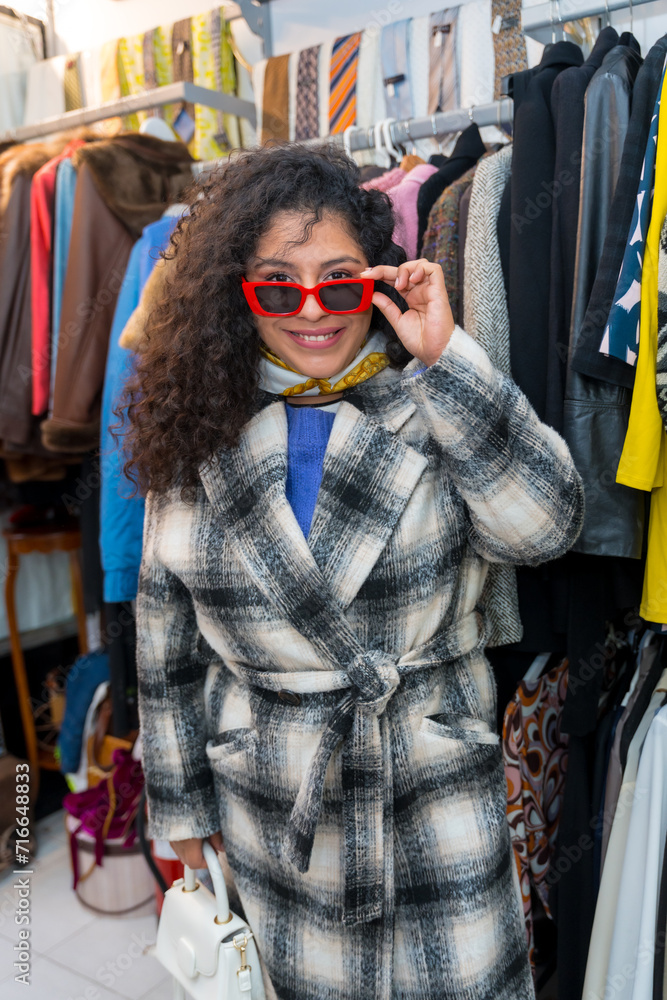 Fototapeta premium Woman looking trough sunglasses shopping in a vintage clothes store