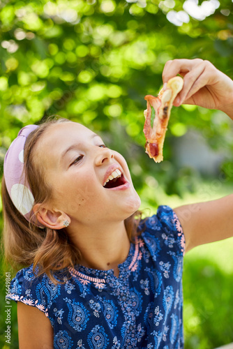 Young Girl Enjoying a Slice of Pizza Outdoors on a Sunny Day
