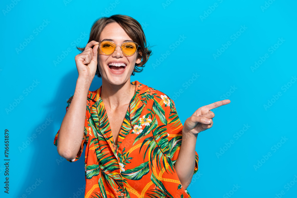 Portrait of nice cheerful person hand touch sunglass indicate finger empty space isolated on blue color background Portrait of nice cheerful person hand touch sunglass indicate finger empty space isolated on blue color background