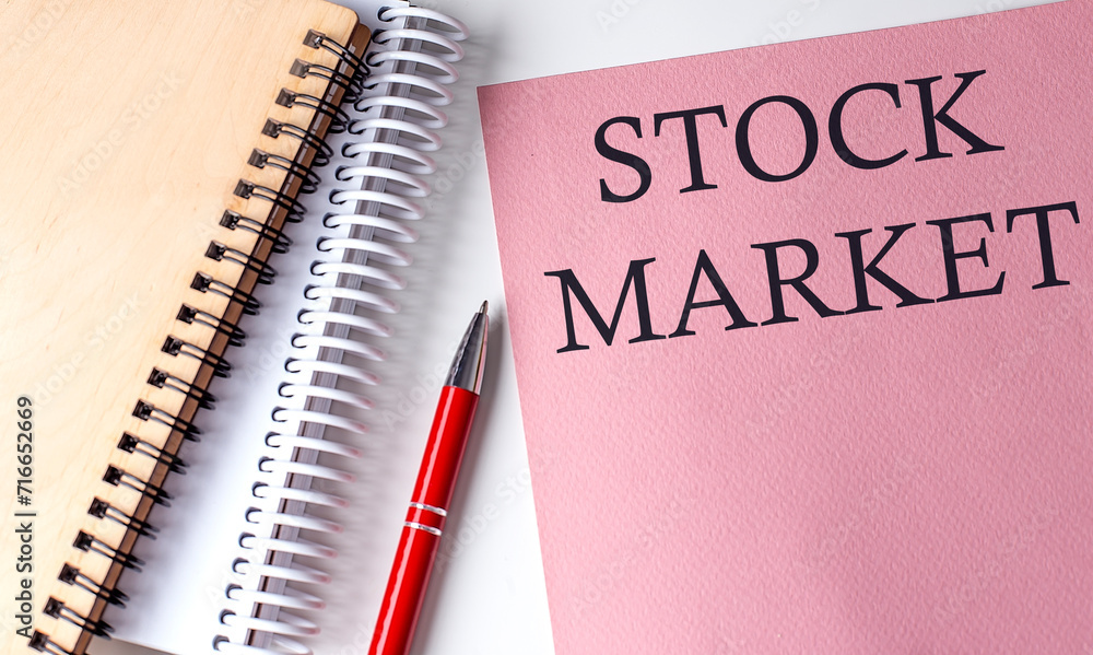 STOCK MARKET word on the pink paper with office tools on white background STOCK MARKET word on the pink paper with office tools on white background