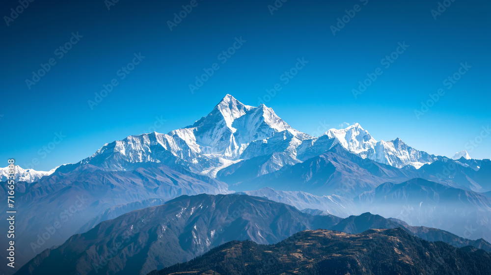 A high-altitude mountain range with snow-capped peaks and clear blue skies.