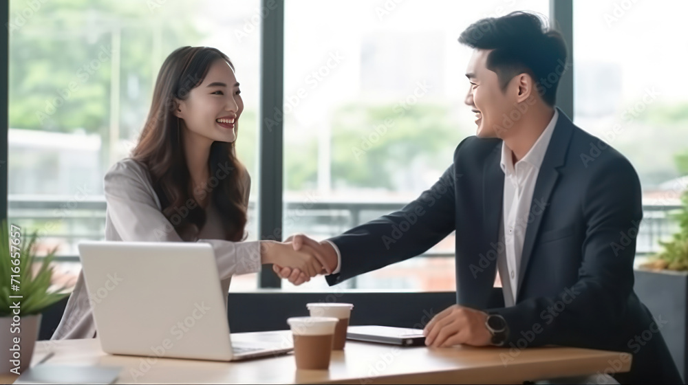 Happy young asian business man and woman shaking hands to congratulate successful collaboration on business deal with documents and laptop on table. Happy young asian business man and woman shaking hands to congratulate successful collaboration on business deal with documents and laptop on table.
