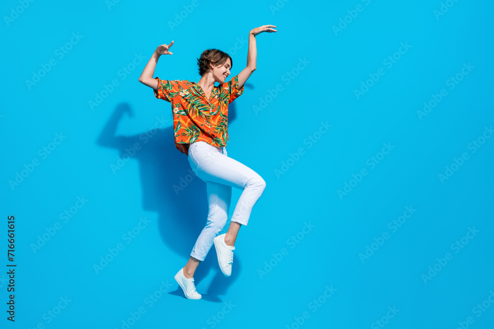 Full length profile portrait of positive lovely person raise arms dancing empty space isolated on blue color background Full length profile portrait of positive lovely person raise arms dancing empty space isolated on blue color background