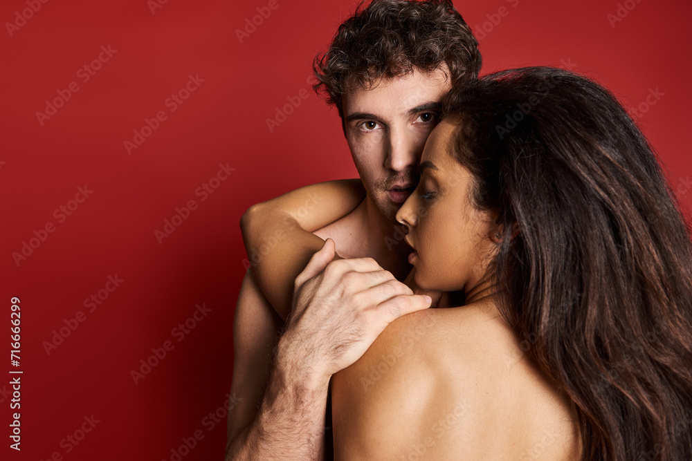 back view of topless young woman with brunette hair hugging muscular man in red background back view of topless young woman with brunette hair hugging muscular man in red background
