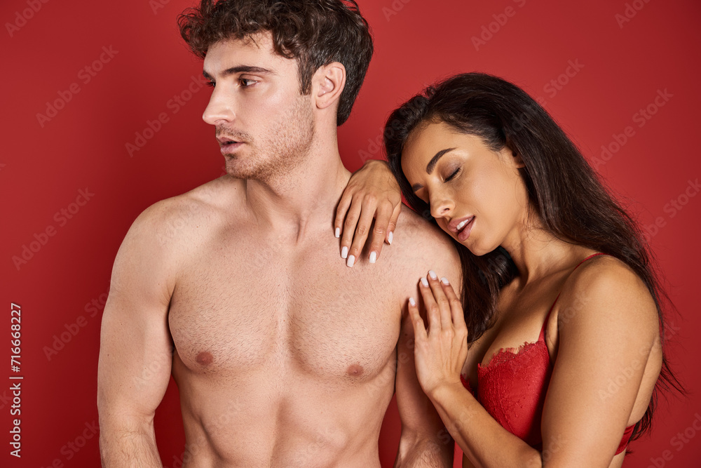 sensual young woman with brunette hair leaning on shirtless man on red background, affection sensual young woman with brunette hair leaning on shirtless man on red background, affection
