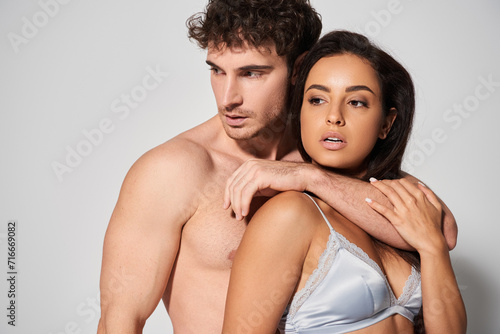 sexy and shirtless man hugging seductive young and pretty woman on grey background, togetherness