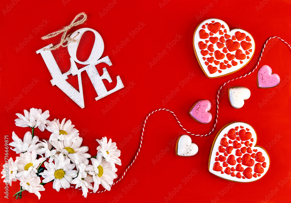 Obraz premium Happy Valentine's Day greeting card. Two gingerbreads in the form of hearts and white chrysanthemum flowers on a red background.