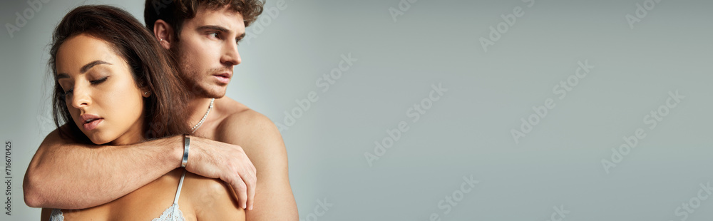 handsome muscular man embracing beautiful young woman in silk bra  on grey background, affection - obrazy, fototapety, plakaty 