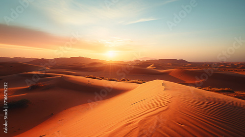 A vast desert landscape at sunset with dunes and sparse vegetation.